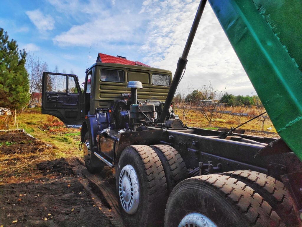 Big green cargo dump truck car with body up on village road in countryside field